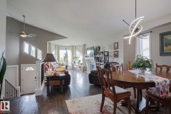 Open-concept living and dining areas with wood-finish flooring, a modern chandelier, a ceiling fan, and a fireplace with a decorative mantel - 