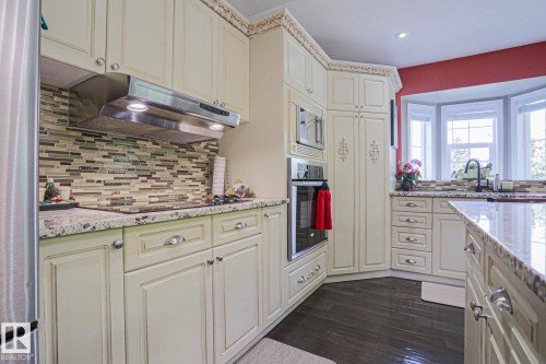 Kitchen featuring cream-colored cabinetry, stone countertops, stainless steel appliances, a tile backsplash, and wood-finish flooring - 3815 41 Street Nw, Edmonton, AB 