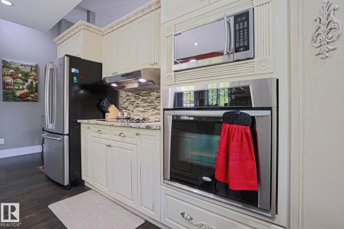 Cream-colored cabinetry with decorative molding, stainless steel built-in microwave, and a stainless steel built-in oven with a glass door - 3815 41 Street Nw, Edmonton, AB 