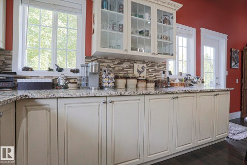 Cream cabinetry featuring glass-front display uppers, speckled countertops, a mosaic tile backsplash, and dark wood-finish flooring - 3815 41 Street Nw, Edmonton, AB 