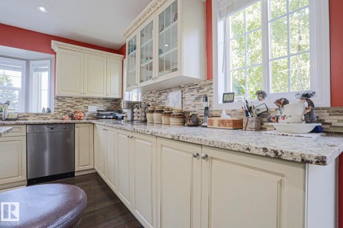 Cream-colored cabinetry with decorative crown molding, stainless steel dishwasher, speckled countertops, and a mosaic tile backsplash - 3815 41 Street Nw, Edmonton, AB 