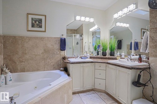 Corner soaking tub, dual vanity with integrated sinks, framed mirrors, stone tile walls, and a separate shower enclosure - 3815 41 Street Nw, Edmonton, AB 