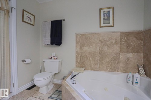 Corner soaking tub with deck-mounted fixtures, stone-tile surround, and tile flooring - 3815 41 Street Nw, Edmonton, AB 
