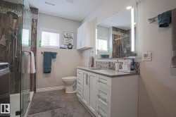 Walk-in shower with glass enclosure and rain showerhead, vanity with undermount sink and stone-finish countertop, illuminated mirror, and mosaic tile backsplash - 