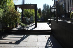 Expansive paver patio with a multi-level wood deck, pergola, and black metal railings - 