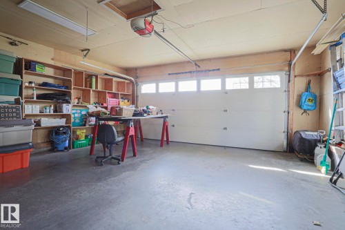 Spacious garage with built-in wooden shelving, a white paneled garage door with windows, concrete flooring, and overhead fluorescent lighting - 3815 41 Street Nw, Edmonton, AB 
