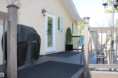 Deck with composite decking, decorative metal railing, a side entry door with window panes, and an exterior wall light fixture - 3815 41 Street Nw, Edmonton, AB 