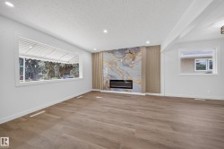 Wood-finish flooring, recessed lighting, expansive window with white trim, linear electric fireplace, and a decorative wall feature with a stone-look panel - 