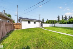 Expansive green lawn with a concrete pathway and a detached white-sided auxiliary building featuring a dark shingle roof and multiple windows - 