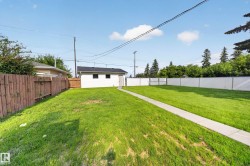 Expansive grassy yard featuring a detached white structure, concrete pathway, and wood fencing - 
