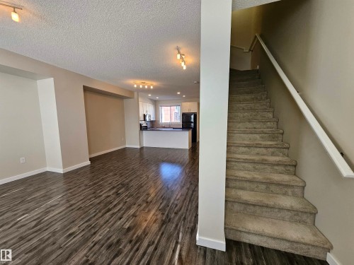 Wood-finish flooring, recessed lighting, white kitchen cabinetry, kitchen island with dark countertop, and carpeted staircase - #69 903 Crystallina Nera Wy Nw, Edmonton, AB 