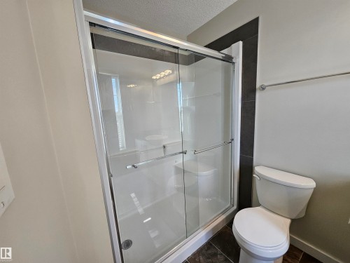 Glass-enclosed shower with sliding doors, white shower surround, dark tile accent wall, and a white toilet - #69 903 Crystallina Nera Wy Nw, Edmonton, AB 