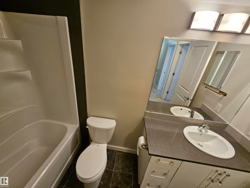 White bathtub with integrated steps, white toilet, dark-toned floor tiling, gray countertop, and a vanity with integrated sink - #69 903 Crystallina Nera Wy Nw, Edmonton, AB 