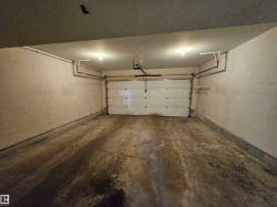 Enclosed garage featuring a concrete floor, overhead lighting, and built-in shelving - 
