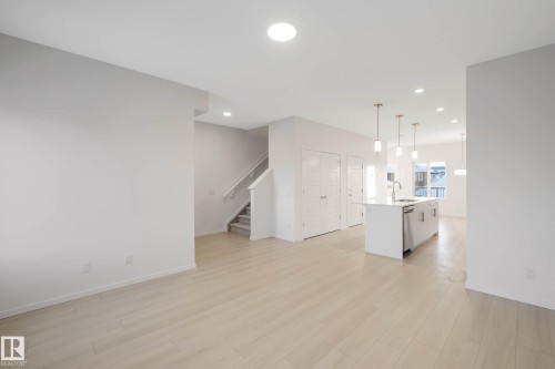 Open-concept living area featuring light wood-finish flooring, recessed lighting, and a kitchen island with an integrated sink and stainless steel dishwasher - 5239 - 5245 21A Avenue Sw, Edmonton, AB 