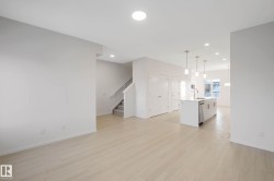 Open-concept living area featuring light wood-finish flooring, recessed lighting, and a kitchen island with an integrated sink and stainless steel dishwasher - 