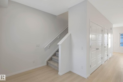 Carpeted staircase with a white handrail, light wood-finish flooring, and white paneled doors - 5239 - 5245 21A Avenue Sw, Edmonton, AB 