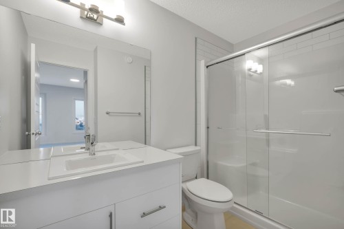 White vanity with integrated sink, glass-enclosed shower with sliding door, and horizontal tile detailing - 5239 - 5245 21A Avenue Sw, Edmonton, AB 
