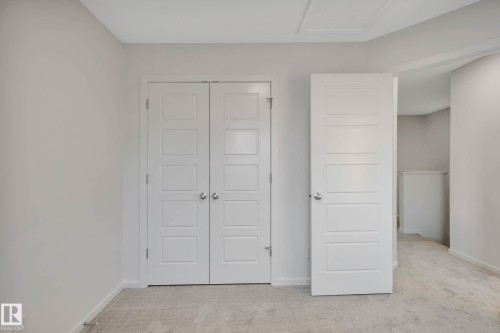 Neutral-toned walls with carpet flooring, featuring a bifold closet door and a paneled interior door - 5239 - 5245 21A Avenue Sw, Edmonton, AB 
