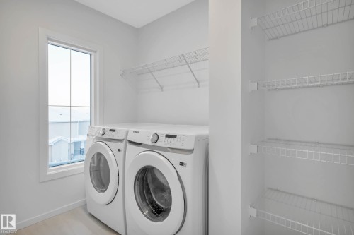 Dedicated laundry area featuring a large window, wire shelving, and wood-finish flooring - 5239 - 5245 21A Avenue Sw, Edmonton, AB 