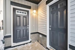 Two paneled entry doors with transom windows, light gray siding, and an exterior wall lantern - 