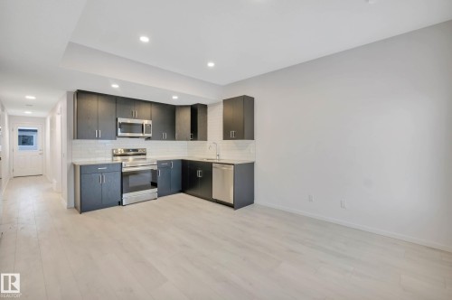 Contemporary kitchen featuring stainless steel appliances, dark cabinetry, light countertops, and a subway tile backsplash - 5239 - 5245 21A Avenue Sw, Edmonton, AB 