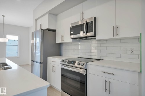 White cabinetry with brushed nickel hardware, stainless steel appliances, white subway tile backsplash, and light-toned countertops - 5239 - 5245 21A Avenue Sw, Edmonton, AB 