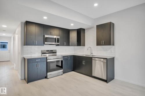 Kitchen featuring dark wood-finish cabinetry, stainless steel appliances, white subway tile backsplash, and light-toned wood-finish flooring - 5239 - 5245 21A Avenue Sw, Edmonton, AB 