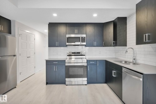 Kitchen featuring dark wood-finish cabinetry, stainless steel appliances, light countertops, and subway tile backsplash - 5239 - 5245 21A Avenue Sw, Edmonton, AB 
