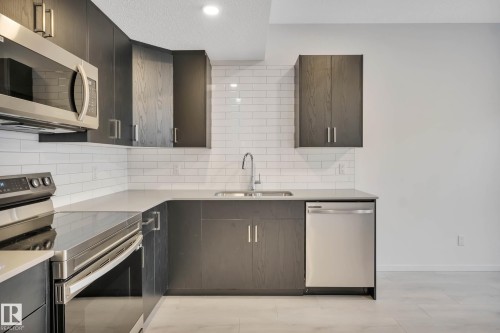 Kitchen featuring dark wood-finish cabinetry, stainless steel appliances, light-colored countertops, a subway tile backsplash, and recessed lighting - 5239 - 5245 21A Avenue Sw, Edmonton, AB 