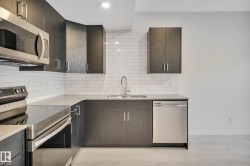 Kitchen featuring dark wood-finish cabinetry, stainless steel appliances, light-colored countertops, a subway tile backsplash, and recessed lighting - 