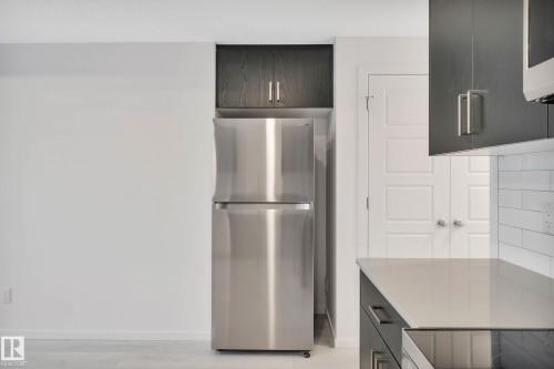 Stainless steel refrigerator, dark wood-finish cabinetry, white subway tile backsplash, light-toned countertop, and modern white paneled door - 5239 - 5245 21A Avenue Sw, Edmonton, AB 