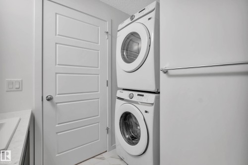 White stackable washer and dryer, white paneled door, light-colored countertop, and light-colored flooring - 5239 - 5245 21A Avenue Sw, Edmonton, AB 
