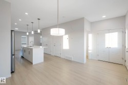 Wood-finish flooring, recessed lighting, and a white kitchen island with an integrated sink and stainless steel appliances - 