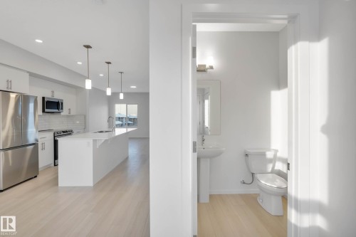 Open-concept kitchen with stainless steel appliances, white cabinetry, a spacious island, and pendant lighting - 5239 - 5245 21A Avenue Sw, Edmonton, AB 