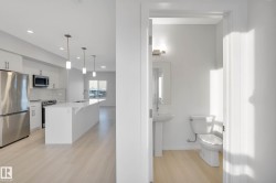 Open-concept kitchen with stainless steel appliances, white cabinetry, a spacious island, and pendant lighting - 