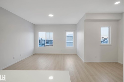 Spacious living area featuring light wood-finish flooring, multiple windows, recessed lighting, and a white countertop visible in the foreground - 5239 - 5245 21A Avenue Sw, Edmonton, AB 