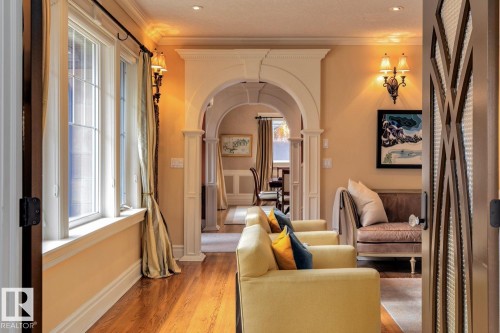 Living area featuring arched walkways, light wood-style flooring, crown molding, and ornate columns - 6306 111 Avenue Nw, Edmonton, AB 