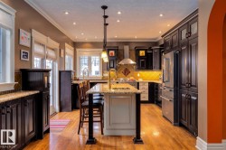 Kitchen with a breakfast bar area, a center island with sink, light stone counters, high end appliances, and hanging light fixtures - 