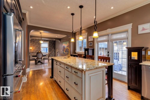 Kitchen with light stone counters, a kitchen breakfast bar, a kitchen island with sink, stainless steel appliances, and crown molding - 6306 111 Avenue Nw, Edmonton, AB 
