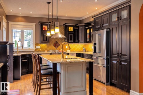 Kitchen with tasteful backsplash, appliances with stainless steel finishes, light stone countertops, pendant lighting, and glass insert cabinets - 6306 111 Avenue Nw, Edmonton, AB 