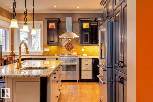 Kitchen with light stone counters, wall chimney exhaust hood, premium appliances, crown molding, and decorative backsplash - 6306 111 Avenue Nw, Edmonton, AB 