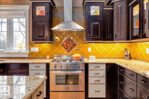 Kitchen featuring dark brown cabinetry, extractor fan, stainless steel stove, and glass insert cabinets - 6306 111 Avenue Nw, Edmonton, AB 