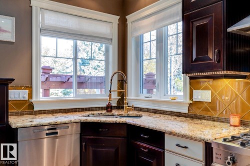 Kitchen with decorative backsplash, dark brown cabinetry, dishwasher, and light stone countertops - 6306 111 Avenue Nw, Edmonton, AB 