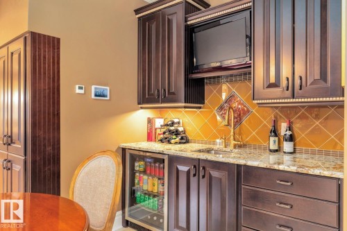 Indoor bar with dark brown cabinets, light stone countertops, backsplash, and beverage cooler - 6306 111 Avenue Nw, Edmonton, AB 