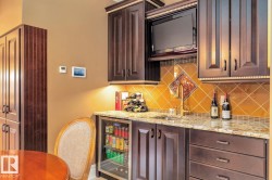 Indoor bar with dark brown cabinets, light stone countertops, backsplash, and beverage cooler - 