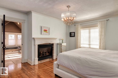 Bedroom featuring a textured ceiling, wood finished floors, a glass covered fireplace, multiple windows, and ornamental molding - 6306 111 Avenue Nw, Edmonton, AB 