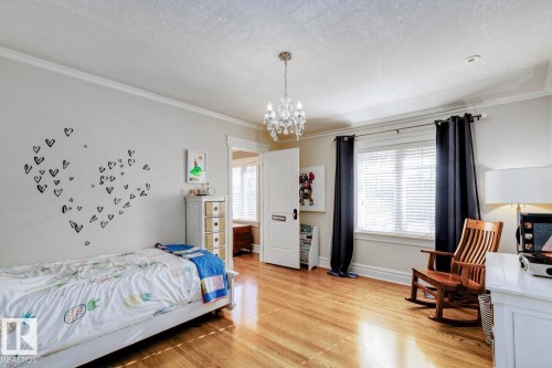 Bedroom featuring light wood finished floors, ornamental molding, a textured ceiling, and a chandelier - 6306 111 Avenue Nw, Edmonton, AB 