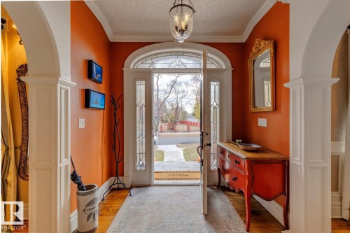Foyer with arched walkways, light wood-style floors, decorative columns, ornamental molding, and a textured ceiling - 6306 111 Avenue Nw, Edmonton, AB 