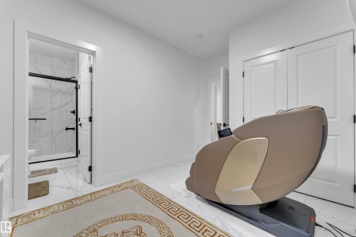 White tile flooring, white walls, double bi-fold closet doors, and an open doorway reveal a white-tiled bathroom with a glass-enclosed shower - 6502 42 Ave, Beaumont, AB 
